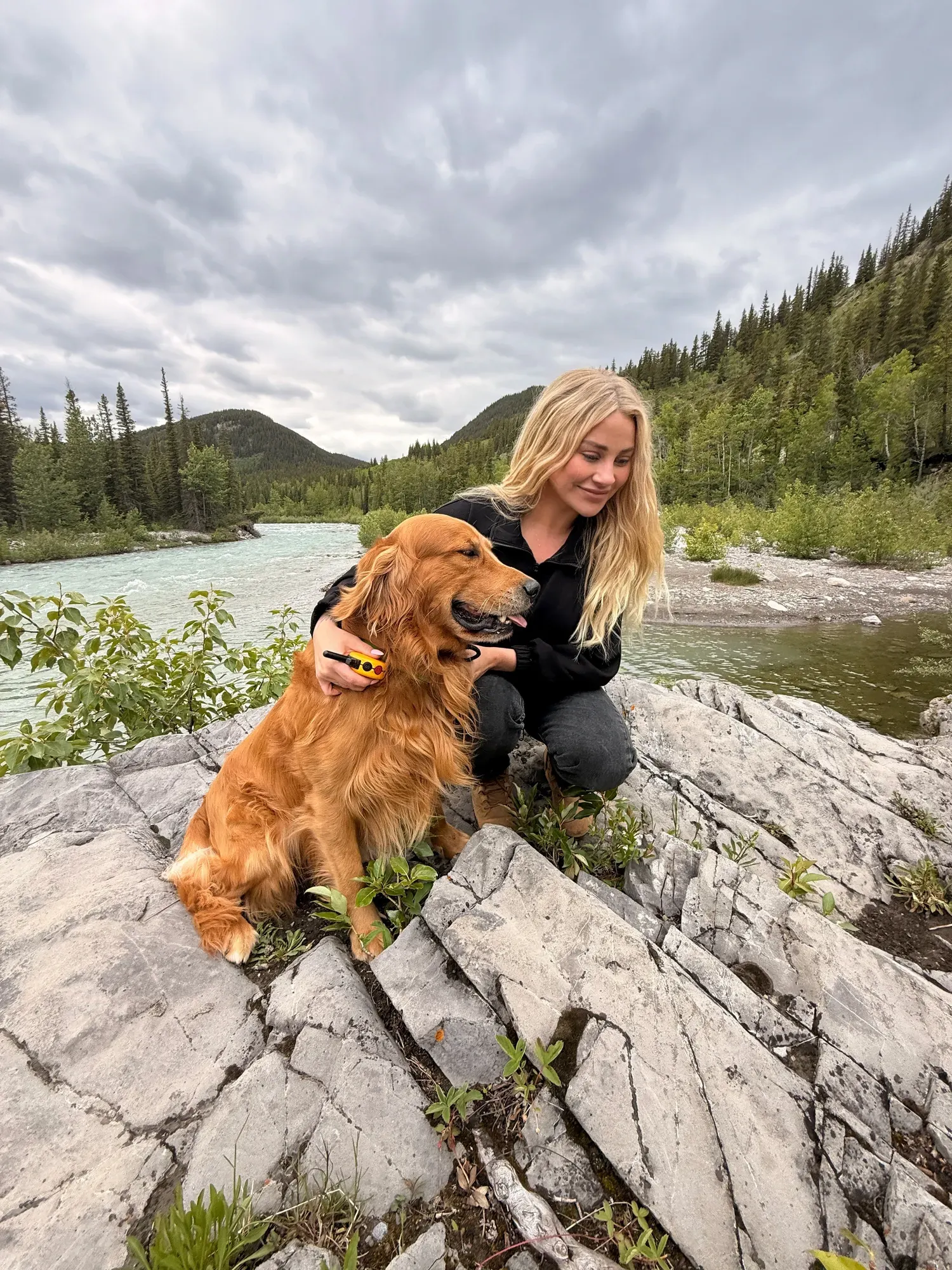 Kaitlin, owner and head trainer of Northline K9, crouched beside a golden retriever on the rocks of a mountain river